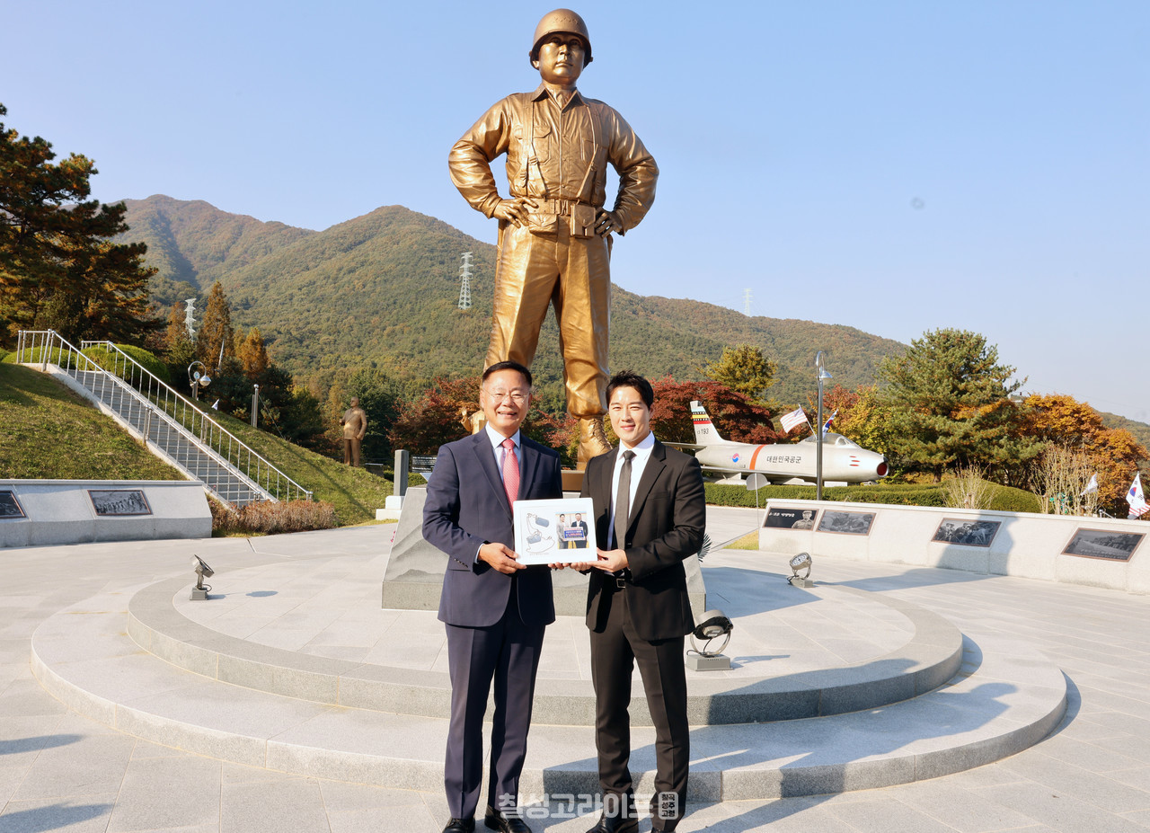 백선엽 장군 동상 앞에서 최영재 마스터가 군번줄로 만든 액자를 전달하고 김재욱 군수와 기념촬영을 하고 있다.